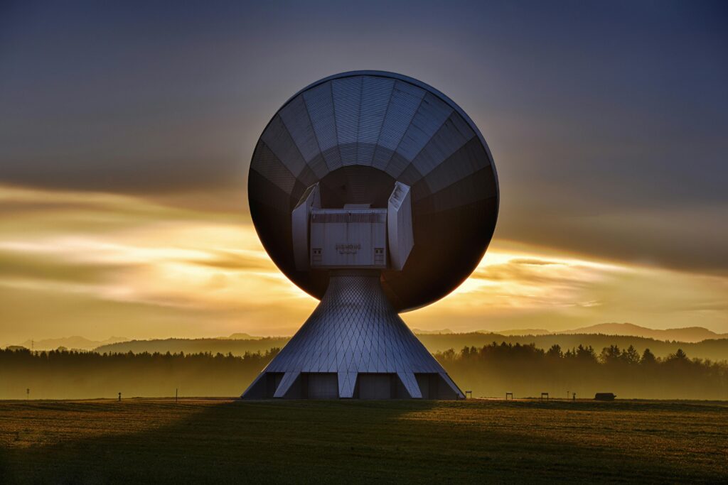 Large satellite dish silhouette against a colorful sunset, showcasing broadcasting technology.